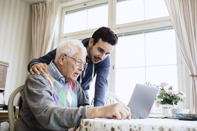 Caretaker and senior man using laptop in nursing home