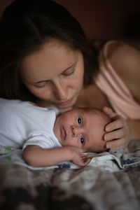 High angle view of cute baby boy lying on bed at home with mother touching