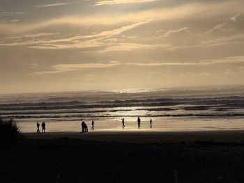Silhouette people at beach against sky during sunset