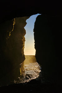 Silhouette rock formation on beach against sky during sunset