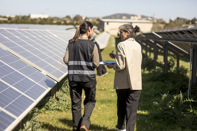 Female entrepreneur discussing with engineer while walking between solar panels at power station