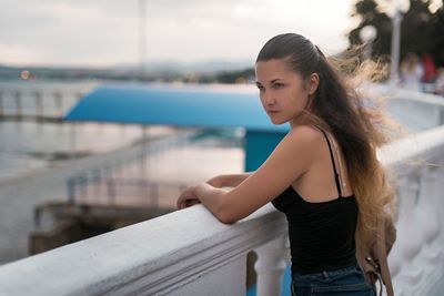 Side view of young woman standing at railing in city