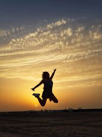 Silhouette woman jumping on beach against sky during sunset