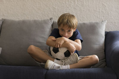Portrait of boy with soccer ball sitting on sofa at home