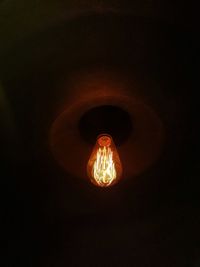 Low angle view of illuminated light bulb in darkroom