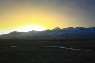 Scenic view of landscape and mountains against cloudy sky during sunset