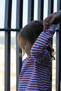 Cropped image of mother holding daughter hand by fence