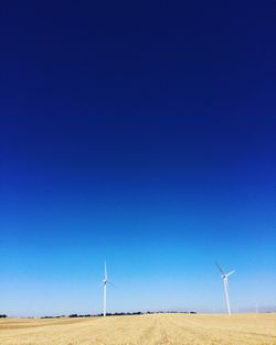 Wind turbines on landscape against blue sky