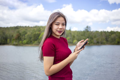Portrait of smiling woman standing by lake against sky
