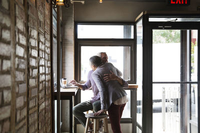 Couple embracing while sitting against windows at cafe