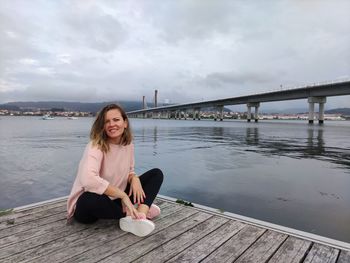 Young woman sitting on bridge over river against sky