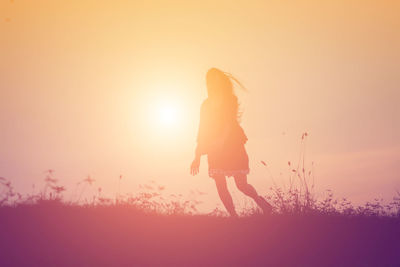 Rear view of silhouette woman standing on field against sky during sunset