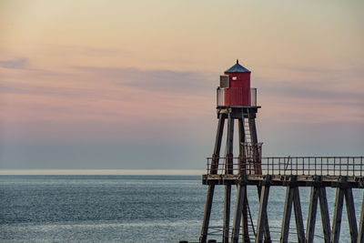 Lighthouse by sea against sky during sunset