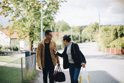 Smiling man and woman talking while walking on street in city during sunny day