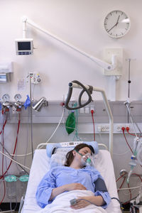 High angle view of female patient wearing oxygen mask while resting on bed in hospital