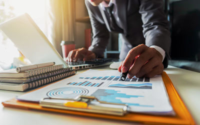 Midsection of businessman pointing on graph while using laptop on table