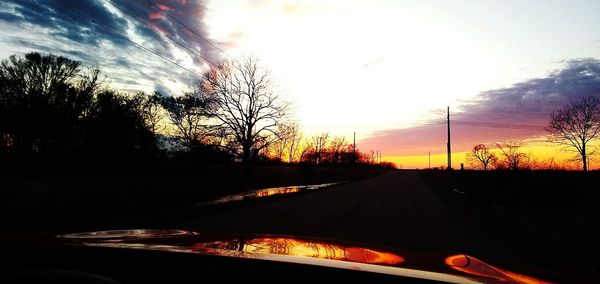 Silhouette trees by road against sky during sunset