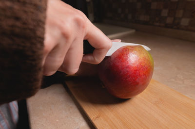 Close-up of woman's hands cutting fresh mango on wooden cutting board at home kitchen