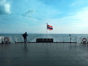 Rear view of man standing in front of thai flag waving on boat sailing in sea