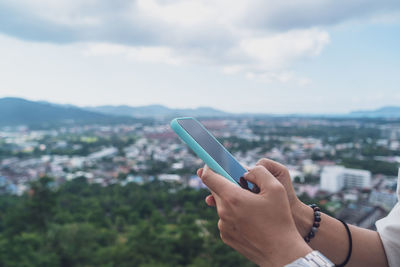 Midsection of person holding mobile phone against sky