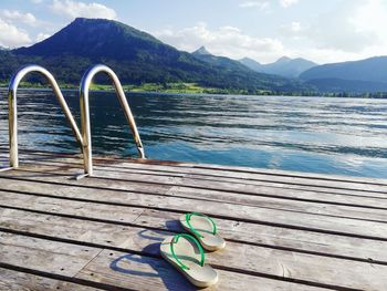 Slippers on pier over lake against mountains