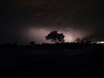 Silhouette trees by road against sky at night