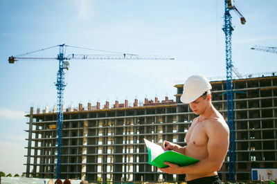 Shirtless man standing against construction buildings