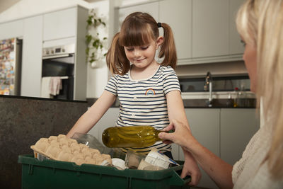 Mother with daughter holding recycling bin at home