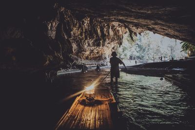 Rear view of man pulling wooden raft with lantern in cave