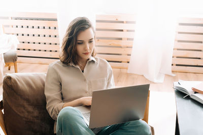 Young woman using laptop while sitting on sofa at home