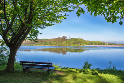 Bench by lake against sky