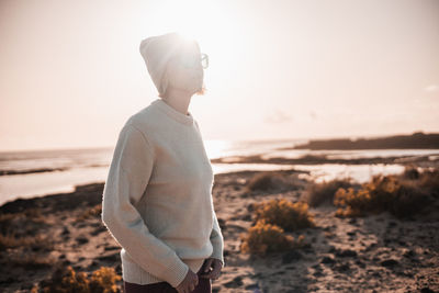 Side view of young man standing on field against sky during sunset