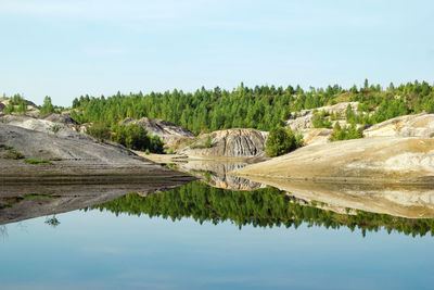 View on a flooded quarry with blue water and reflection of hills and forest.