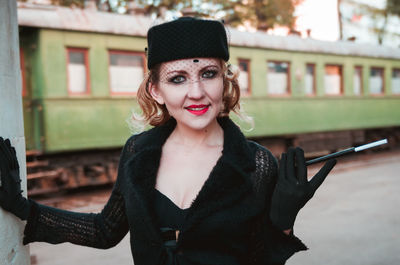 Portrait of smiling woman wearing hat while standing at railroad station