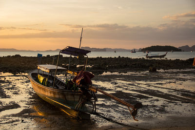 Boat moored on beach against sky during sunset