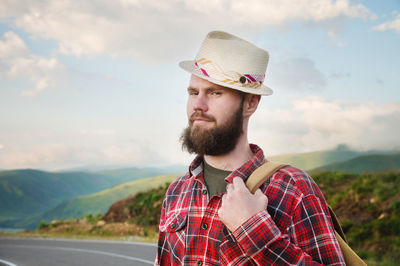 Portrait of a sly cheerful bearded jewish man hitchhiker in a hat and shirt against the backdrop 