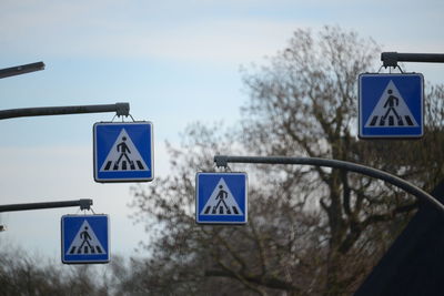 Low angle view of pedestrian crossing signs against sky