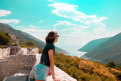 Side view of woman standing by mountain against sky