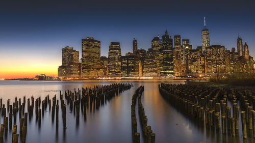 Wooden posts in east river against manhattan skyline during sunset