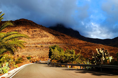 Diminishing perspective of road passing through mountains against cloudy sky