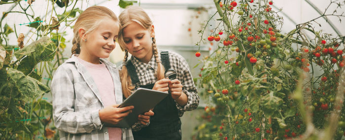 Young woman using phone while standing on plants