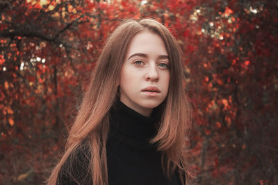 Autumn portrait of a beautiful cute woman against a background of bright red leaves. black sweater