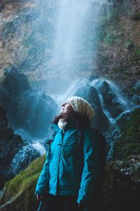 Young man standing by waterfall in forest