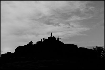 Low angle view of silhouette people standing on rock