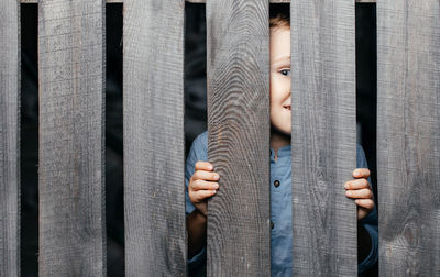 Happy smiling white boy looks out of the crack of a wooden fence. childish curiosity. espionage