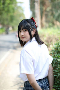 Portrait of young woman standing against trees