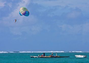 People on floating board with person parasailing against cloudy sky