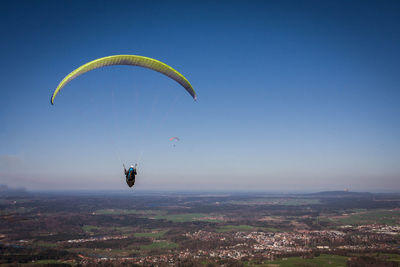 Person paragliding over landscape against clear sky