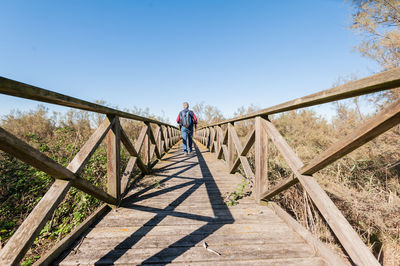 Man walking on footbridge against clear sky