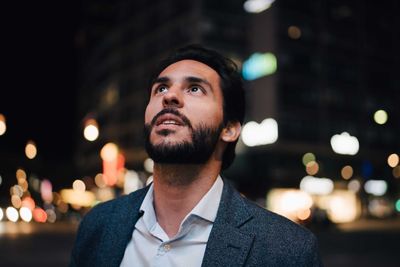 Contemplating man looking up while standing in city at night